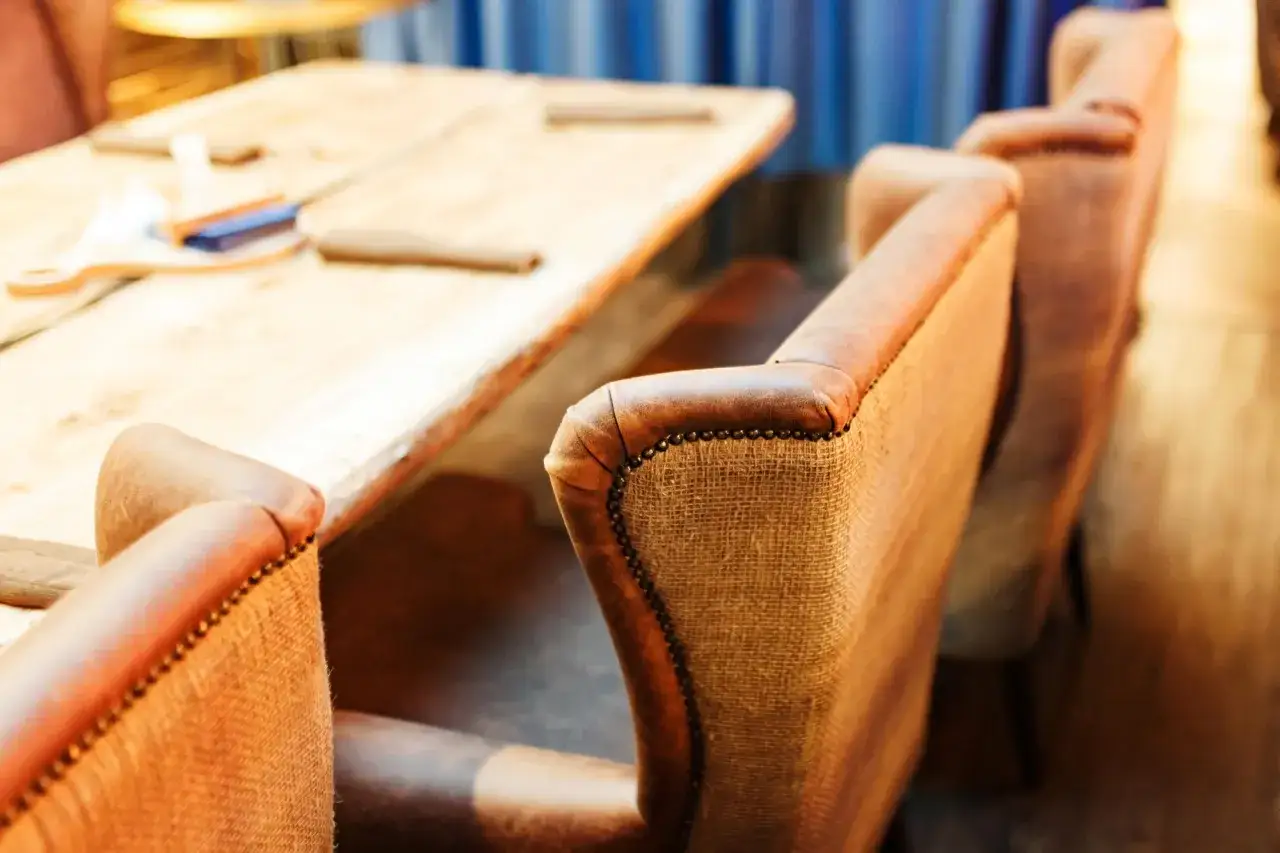 Eleganckie tapicerowanie mebli w restauracji: brązowe fotele z ozdobnymi ćwiekami przy drewnianym stole.