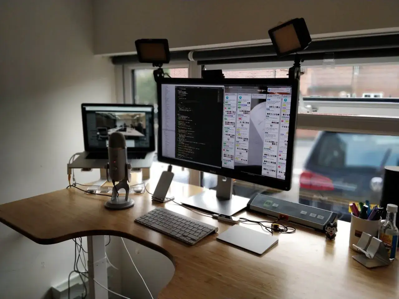 Stanowisko do pracy zdalnej programisty: dwa monitory z kodem, laptop, mikrofon, klawiatura i akcesoria.