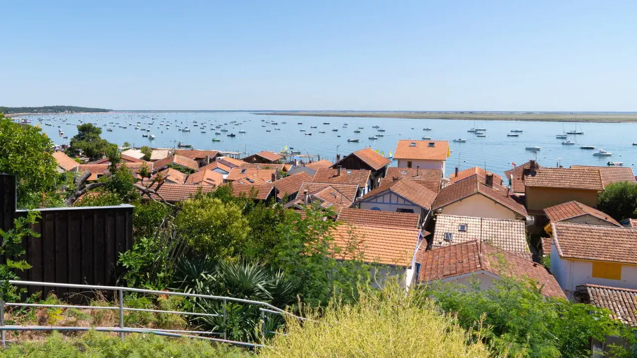 Vue d'un village de pêcheurs et de ses toits orangés, avec une myriade de bateaux sur l'eau bleue. Idéal pour savoir que faire au Cap Ferret.
