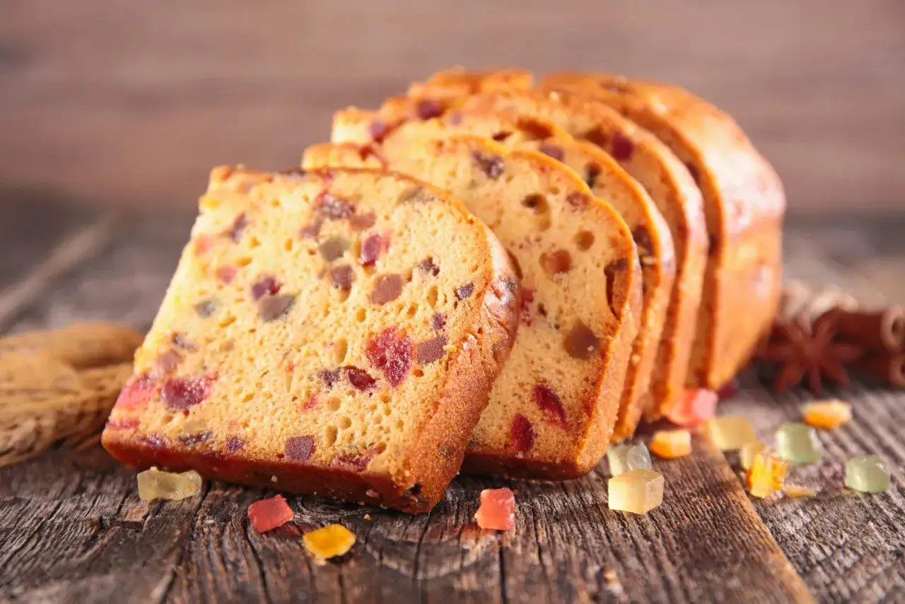 Tranches de g&acirc;teau de voyage aux fruits confits, parsem&eacute;es de bonbons color&eacute;s sur fond de bois.