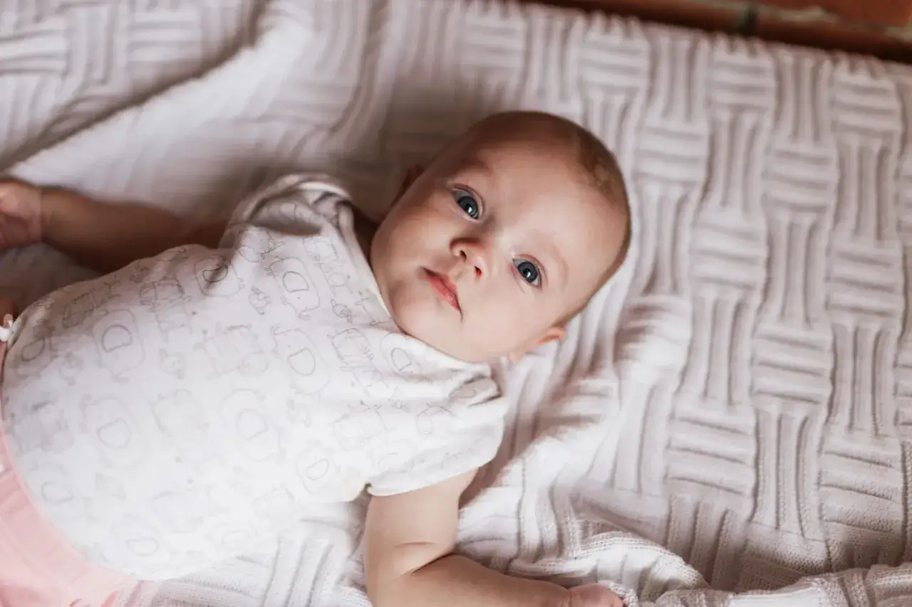 Un b&eacute;b&eacute; aux yeux bleus, pr&eacute;nom en H, porte un body orn&eacute; d'&eacute;l&eacute;phants. Il est allong&eacute; sur une couverture textur&eacute;e.
