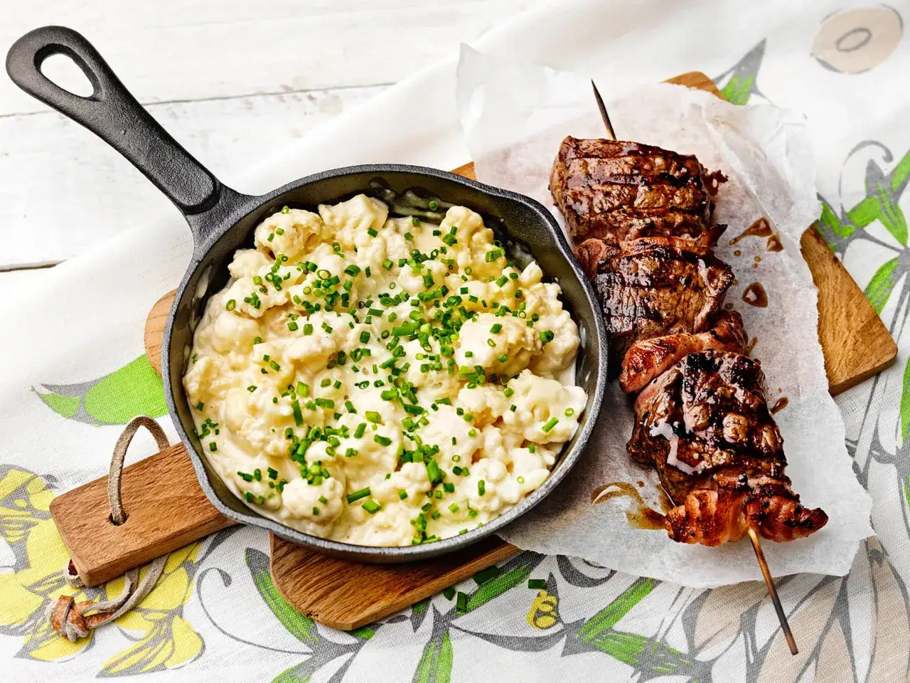 En gjutj&auml;rnspanna med kr&auml;mig stuvad blomk&aring;l toppad med gr&auml;sl&ouml;k bredvid grillspett med saftigt k&ouml;tt.