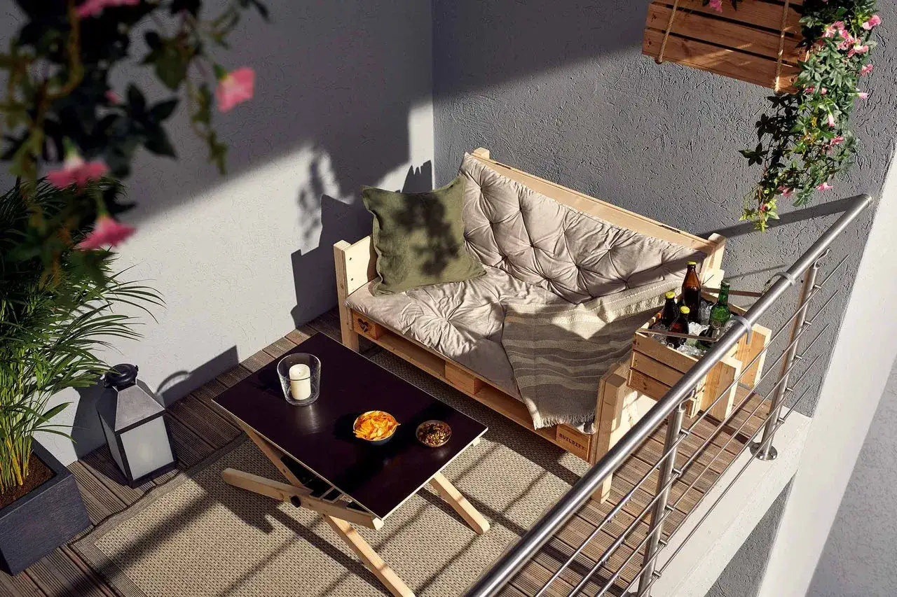 Gemütliche Balkon Ideen: Paletten-Sofa, Holztisch mit Snacks und Getränkekiste. Pflanzen und Lichterkette sorgen für Ambiente.