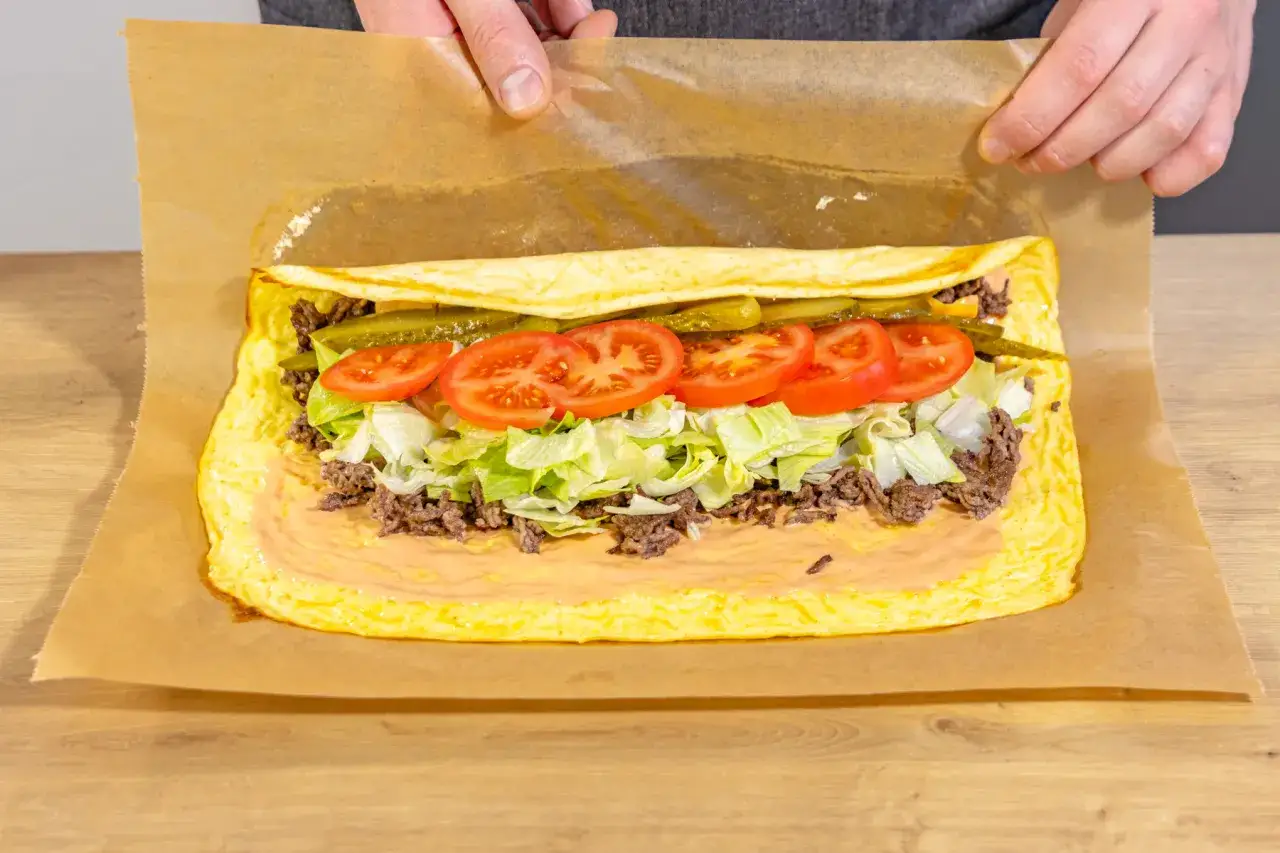 Eine Big Mac Rolle wird mit Hackfleisch, Salat, Tomaten, Gurken und Sauce auf einem Omelett zubereitet.
