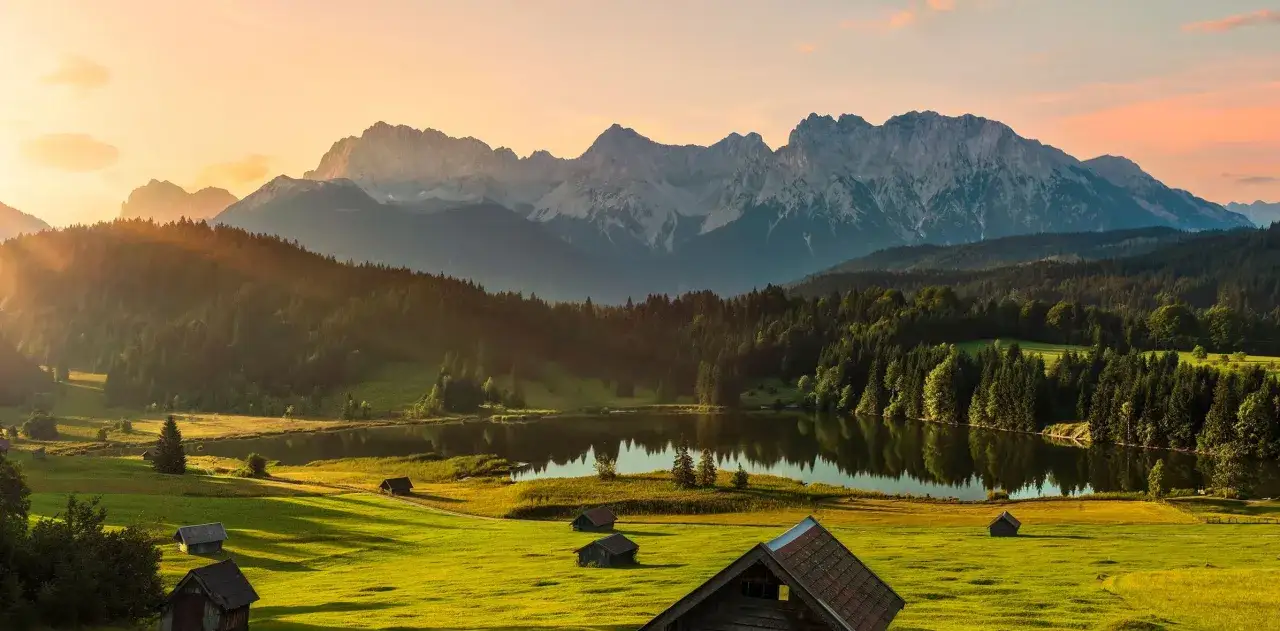 Sonnenuntergang &uuml;ber einem Bergsee mit kleinen H&uuml;tten auf gr&uuml;nen Wiesen. Ein idyllisches Bild, das zu den beliebtesten Urlaubsziele z&auml;hlt.