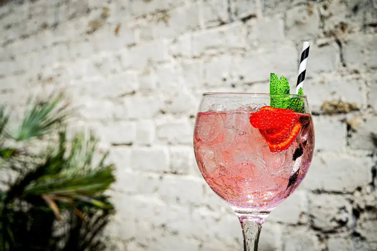 Orzeźwiający gin z różową lemoniadą, ozdobiony truskawką i miętą, na tle ceglanej ściany. Idealny na upalne dni, lepszy niż gin z tonikiem.
