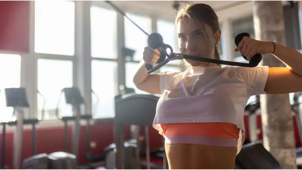Junge Frau trainiert im Fitnessstudio mit einem Kabelzug. Sie führt eine Face Pull-Übung aus, um ihre Schultern und den oberen Rücken zu stärken.
