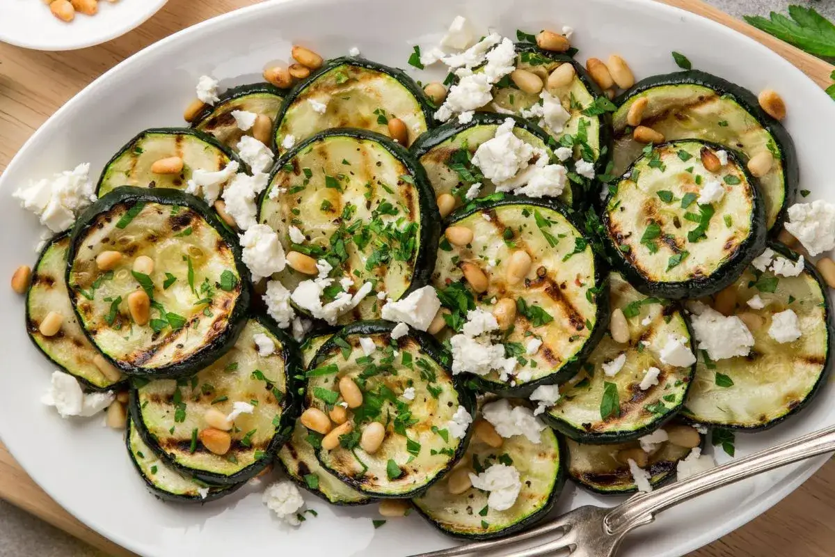 Grillowana cukinia z serem feta i orzeszkami pinii, posypana świeżą natką pietruszki. Pyszne danie na lato.