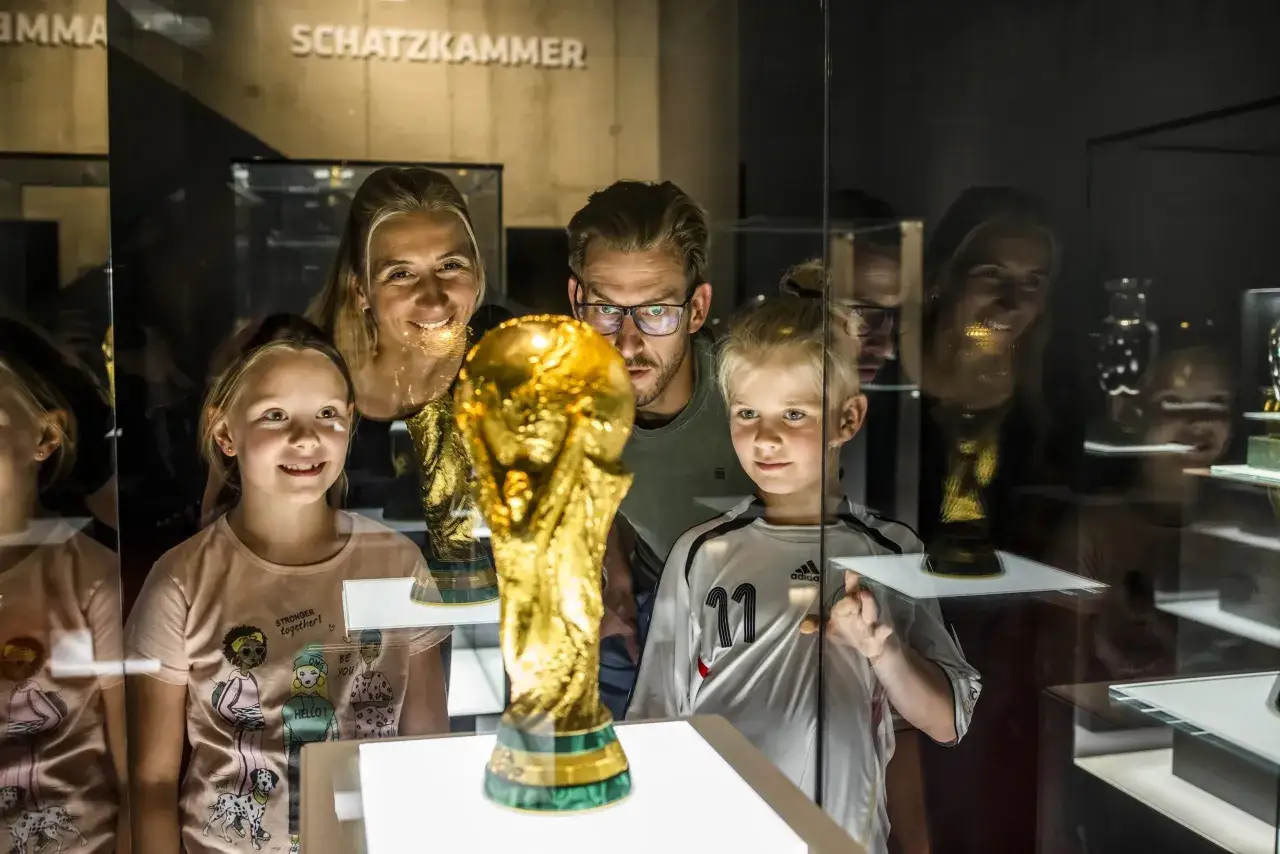 Familie bestaunt den WM-Pokal im Mitmach Museum NRW. Kinder und Eltern blicken fasziniert auf die Trophäe hinter Glas.