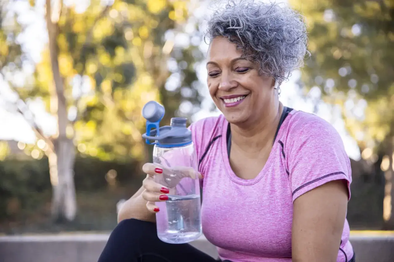 L&auml;chelnde Frau mit Wasserflasche, ein Beispiel f&uuml;r gesunde Lebensweise und obstipation prophylaxe durch Bewegung und Fl&uuml;ssigkeitszufuhr.