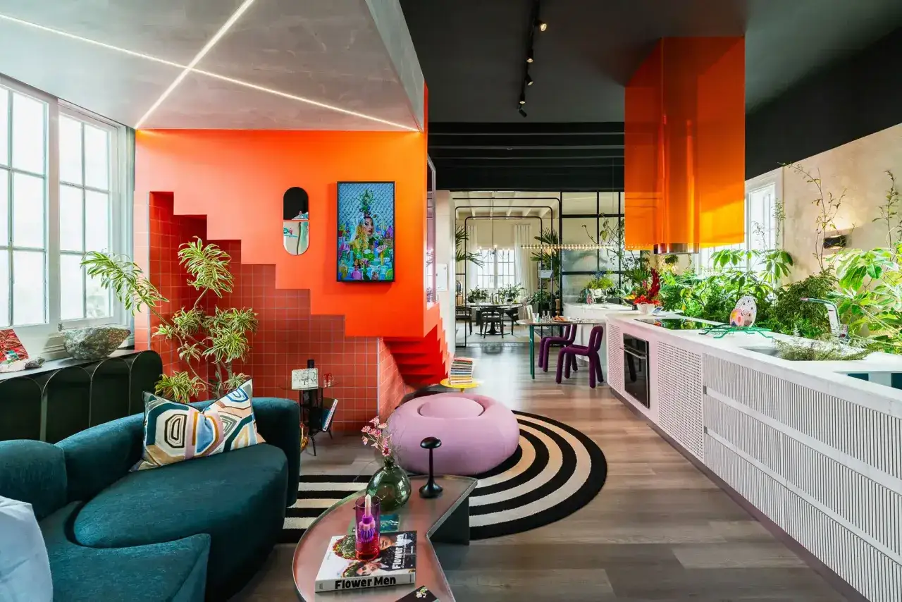 Un espacio vibrante con **dopamine decor**: sofá verde, escaleras naranjas, plantas exuberantes y una campana de cocina naranja brillante.