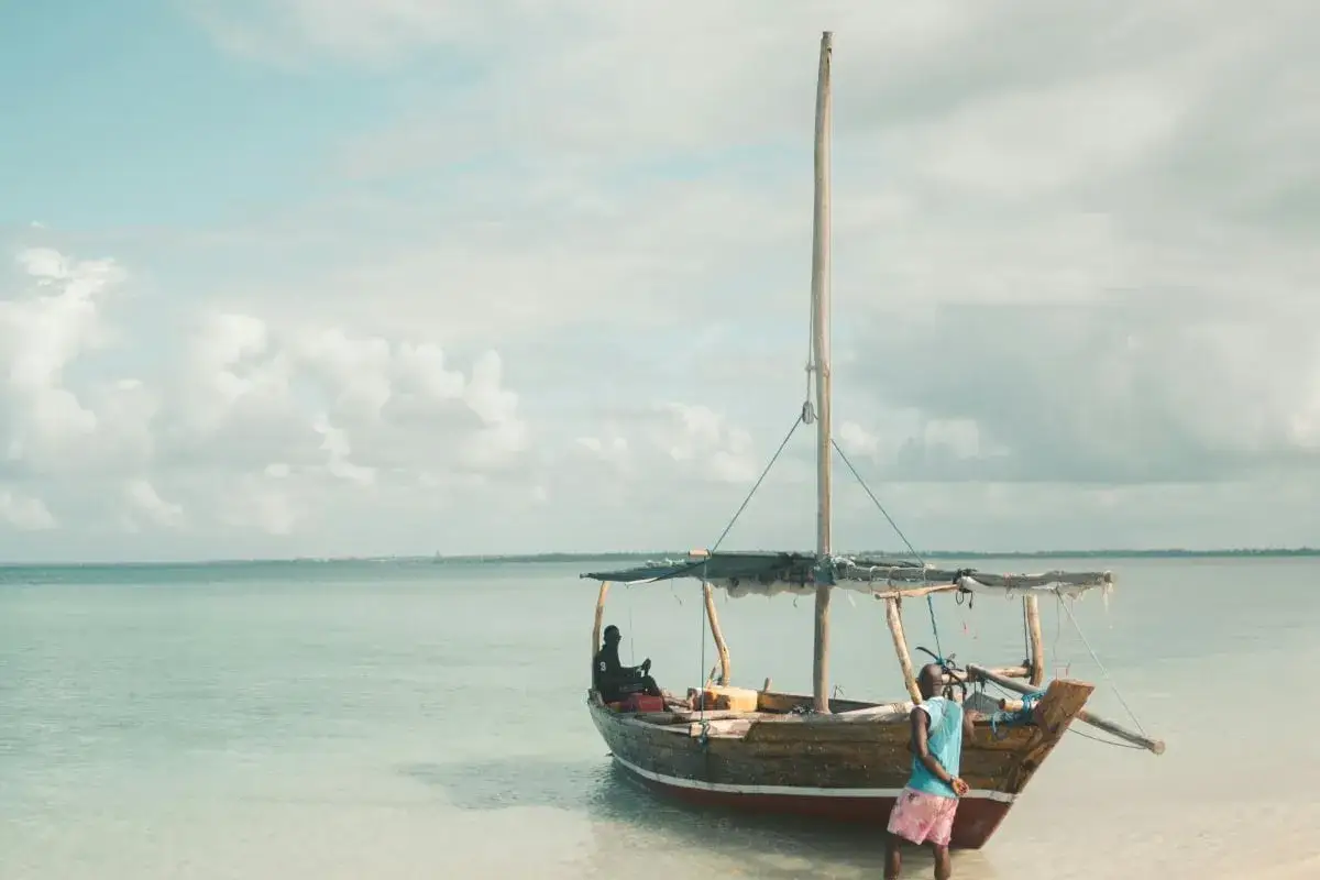 Dhow na plaży na Zanzibarze, gdzie przygotowania do podróży obejmują także zanzibar szczepienia. Dzieci bawią się przy łodzi.