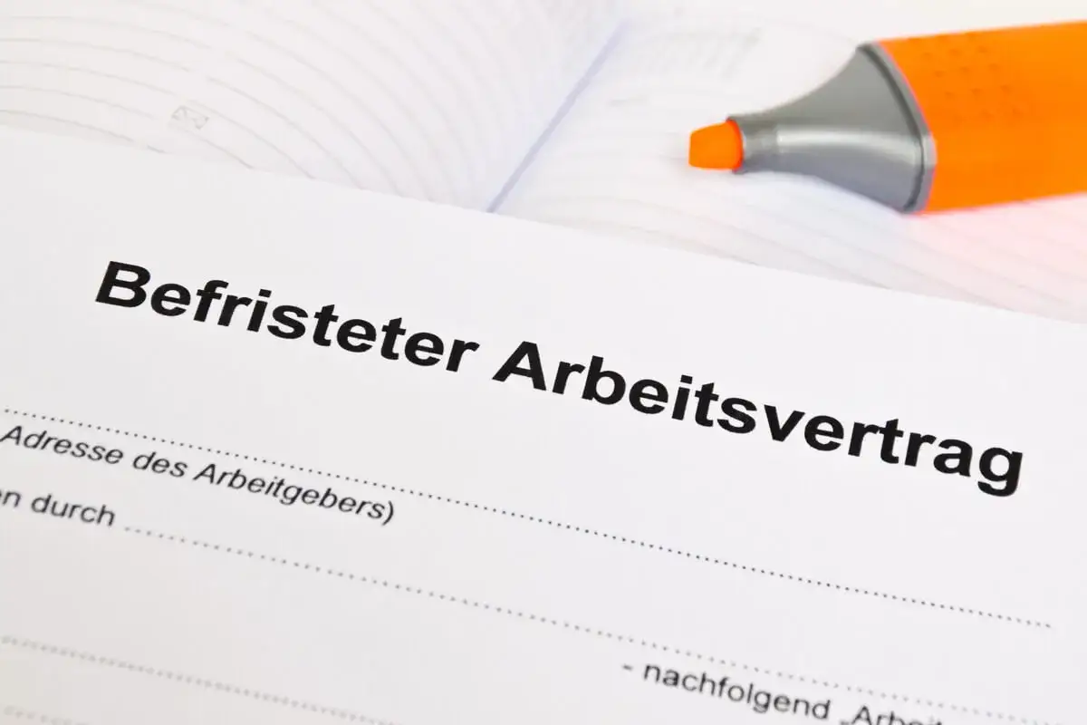 Ein befristeter Arbeitsvertrag liegt auf dem Tisch. Wann muss der Arbeitgeber bescheid geben? Ein orangefarbener Textmarker liegt daneben.