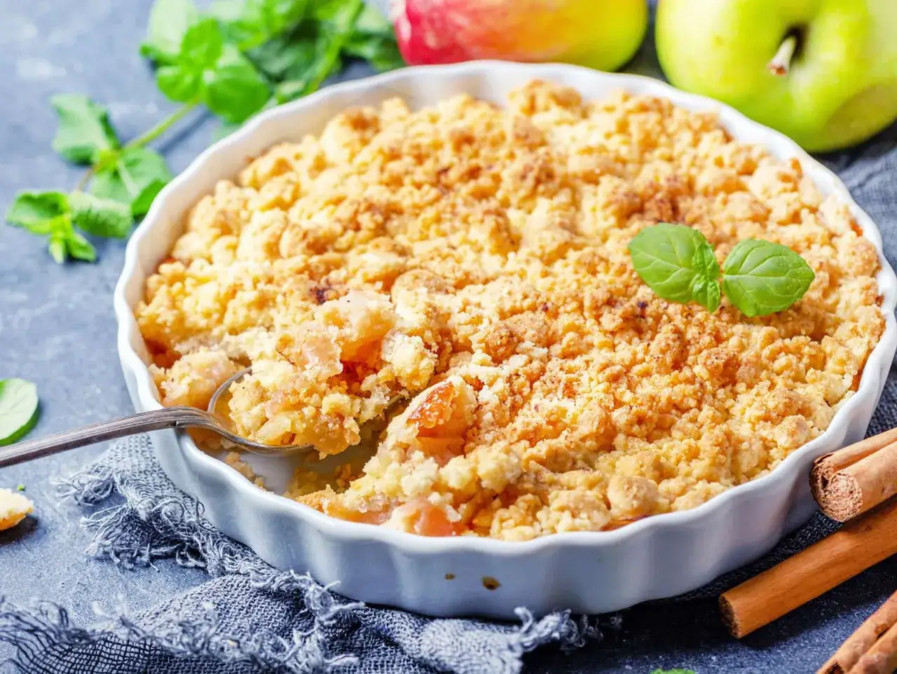 Goldbrauner Apfel-Crumble im Ofen, ein köstliches Rezept für süße Momente. Daneben Äpfel und Zimtstangen.