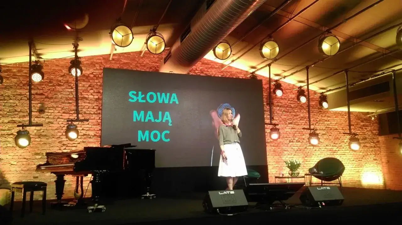 Kobieta przemawia na scenie. Na ekranie napis 
