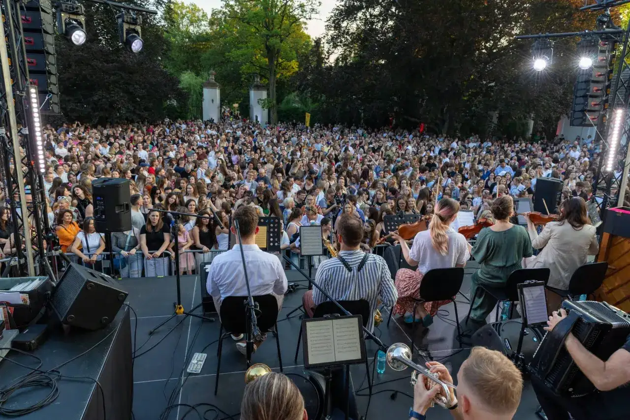 Koncert w Krakowie na weekendowe wydarzenia. Tłum ludzi na koncercie plenerowym, muzycy grają na scenie.