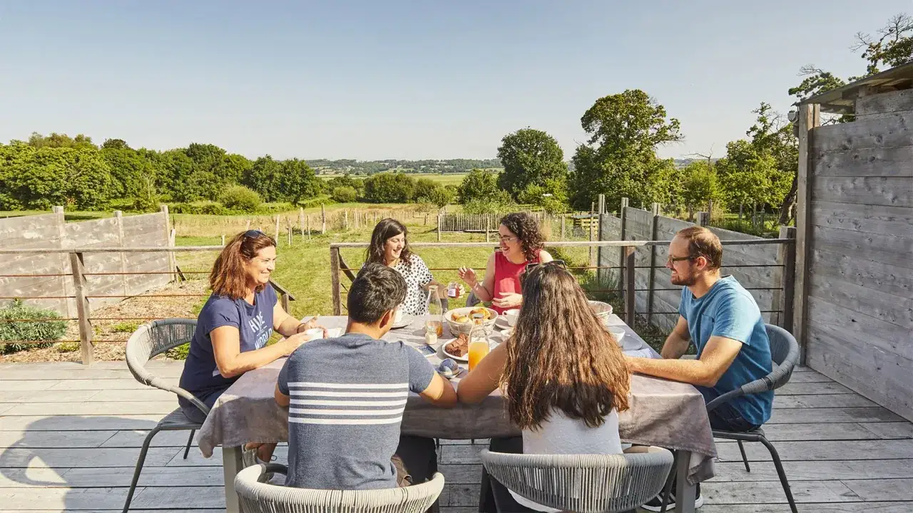 Six amis profitent d'un petit-déjeuner ensoleillé en Bretagne, sur une terrasse avec vue sur la campagne.