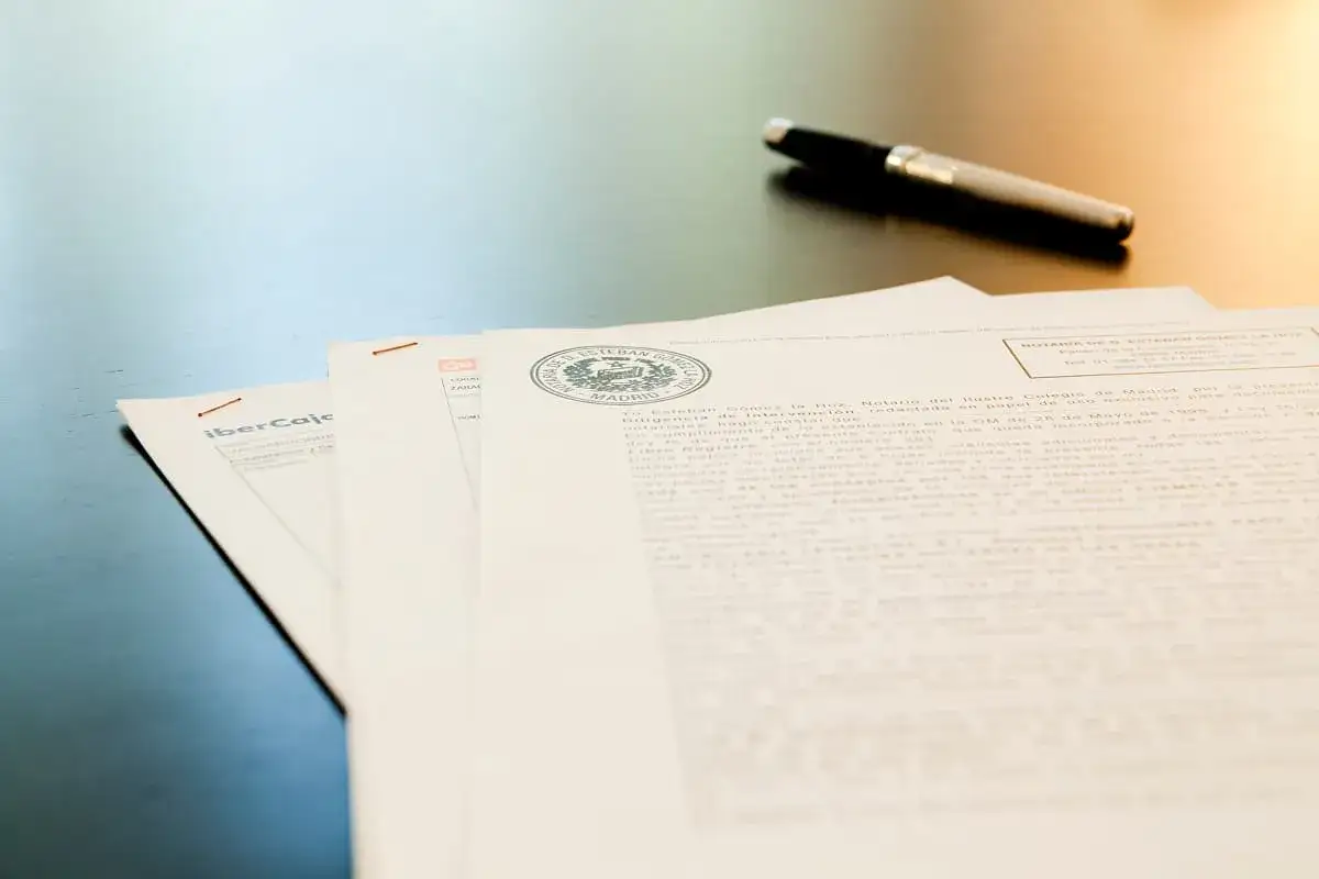 Documentos apilados, un bolígrafo y un sello notarial sugieren los requisitos para pedir una hipoteca.