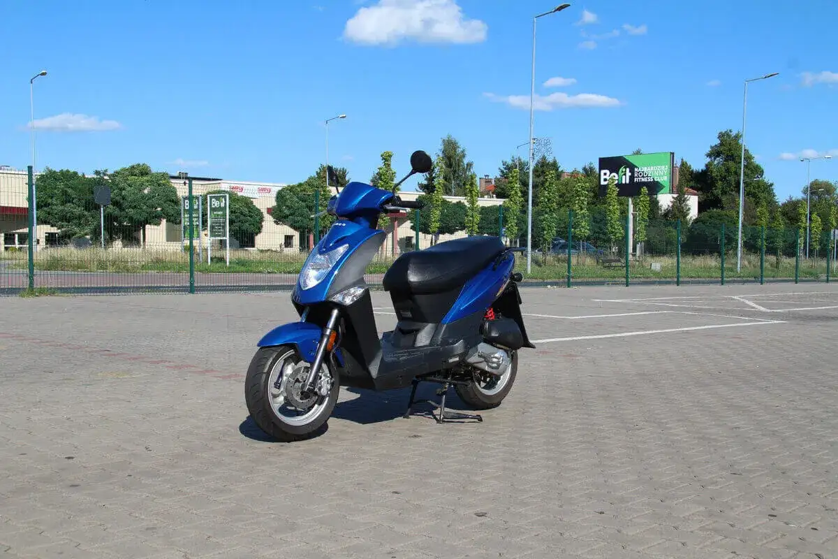 Niebieski skuter stoi na parkingu. Od ilu lat można mieć kartę motorowerową?