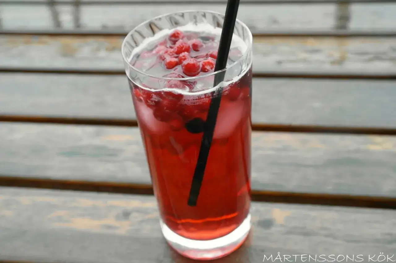 En h&ouml;g glas med en r&ouml;d vargtass drink fylld med is och r&ouml;da b&auml;r, med ett svart sugr&ouml;r.