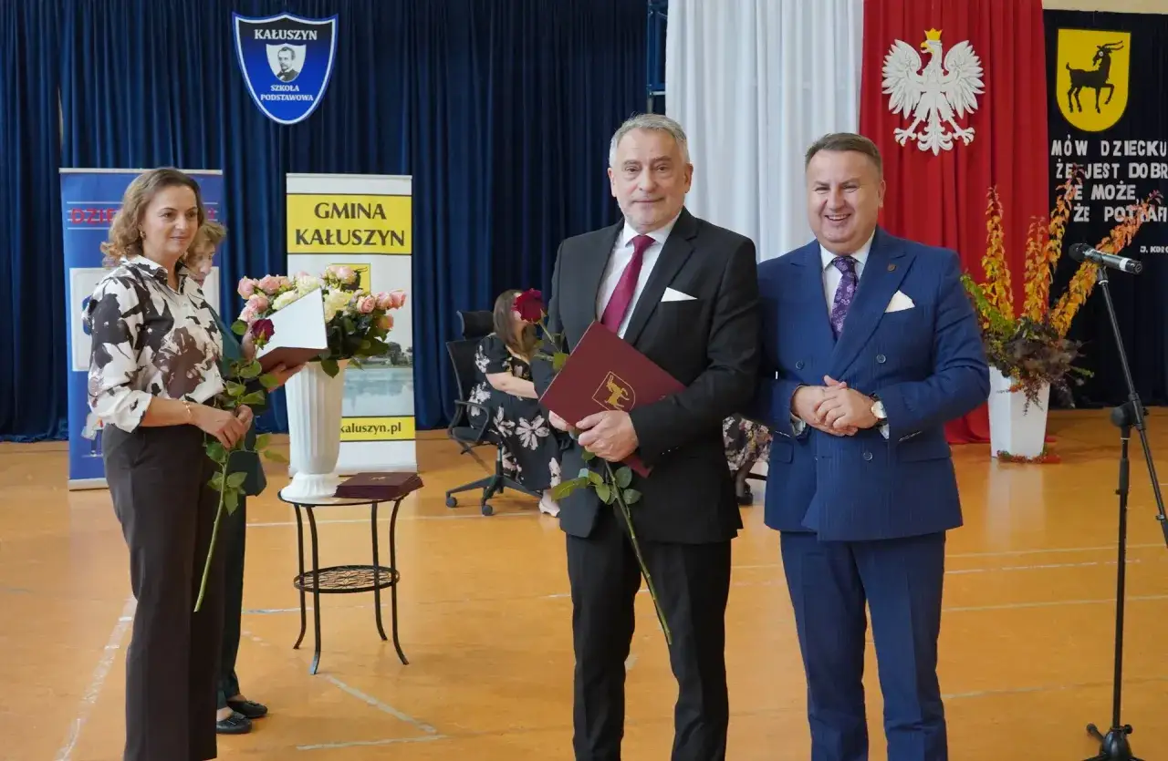 Dyrektor szkoły w garniturze odbiera gratulacje i kwiaty podczas uroczystości.