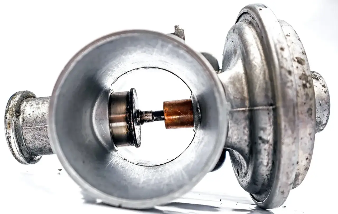 Metalowy mechanizm z miedzianym elementem, przypominający część starego silnika lub pompy. Może to być element z dawnego nagaru.