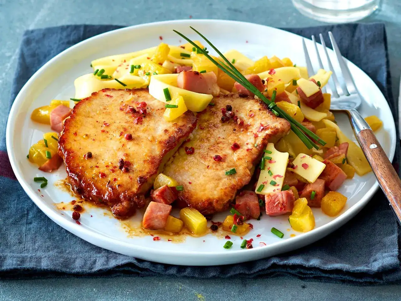 Zwei goldbraune Schnitzel Hawaii mit Ananaswürfeln, Schinken und Käse, garniert mit Schnittlauch und rosa Pfeffer.