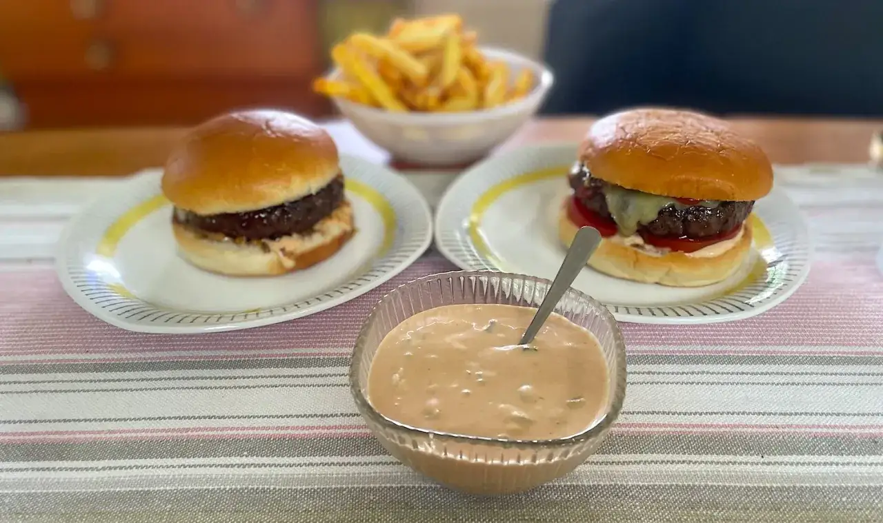 Två saftiga hamburgare med pommes frites och en skål med krämig hamburgerdressing. Perfekt för en mysig hemmakväll!