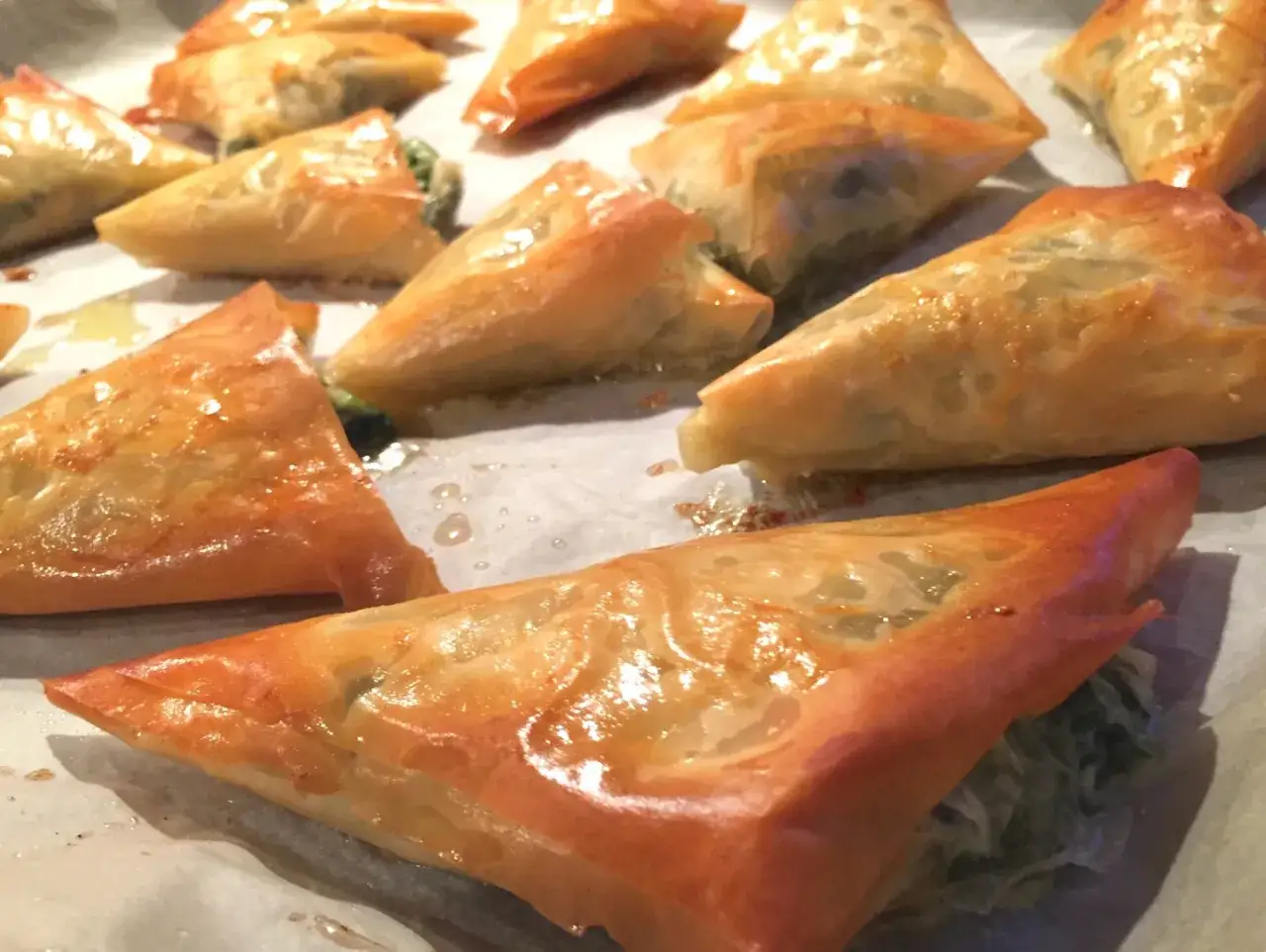 Złociste, chrupiące trójkąty spanakopita, wypełnione szpinakiem i fetą, gotowe do podania.