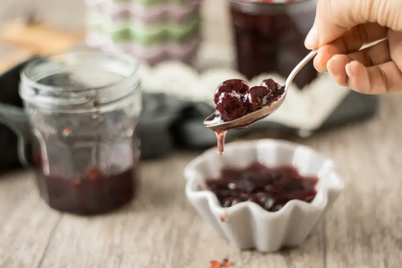 L&ouml;ffel mit Amarena Kirschen, perfekt f&uuml;r ein schnelles Amarena Kirschen Rezept. Daneben ein Glas mit Kirschmarmelade.