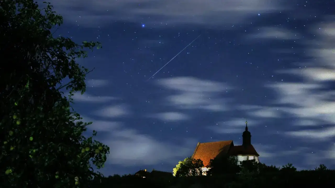Ein Sternschnuppenregen über einer Kirche. Wann sieht man Sternschnuppen? Oft bei klarem Himmel in der Nacht, wie hier.