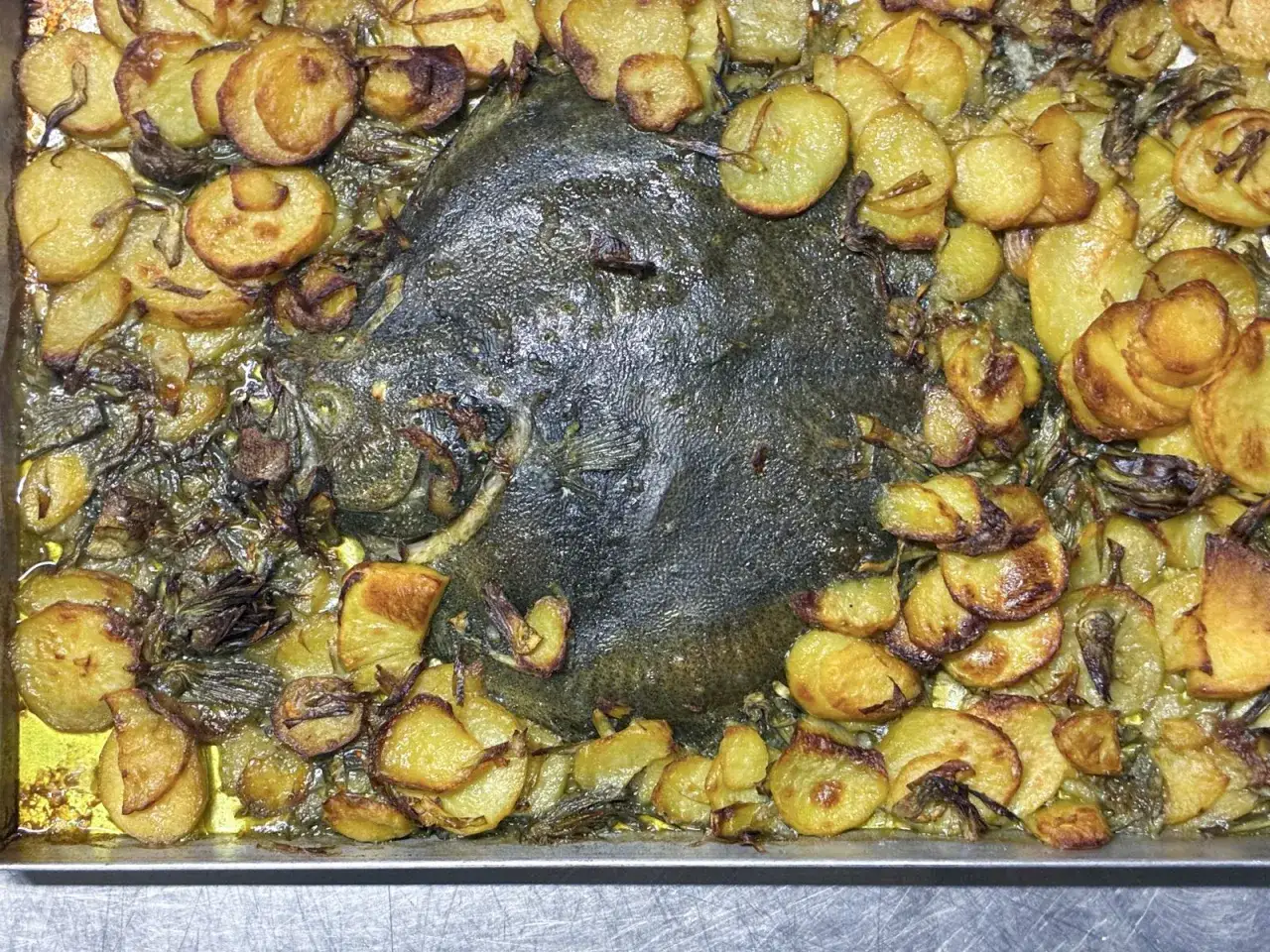 Rombo al forno con patate dorate e cipolle caramellate, un piatto succulento pronto per essere gustato.