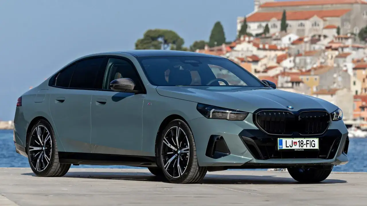 Szary BMW 520 z czarnym grillem i felgami, zaparkowany na tle nadmorskiego miasteczka.
