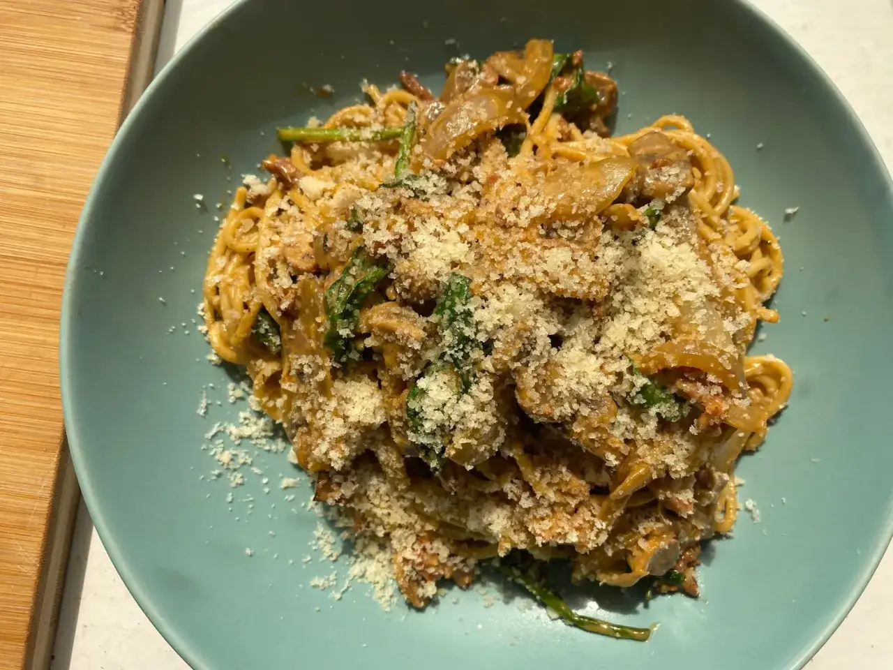 En portion pasta boscaiola med svamp och spenat, toppad med riven parmesanost.