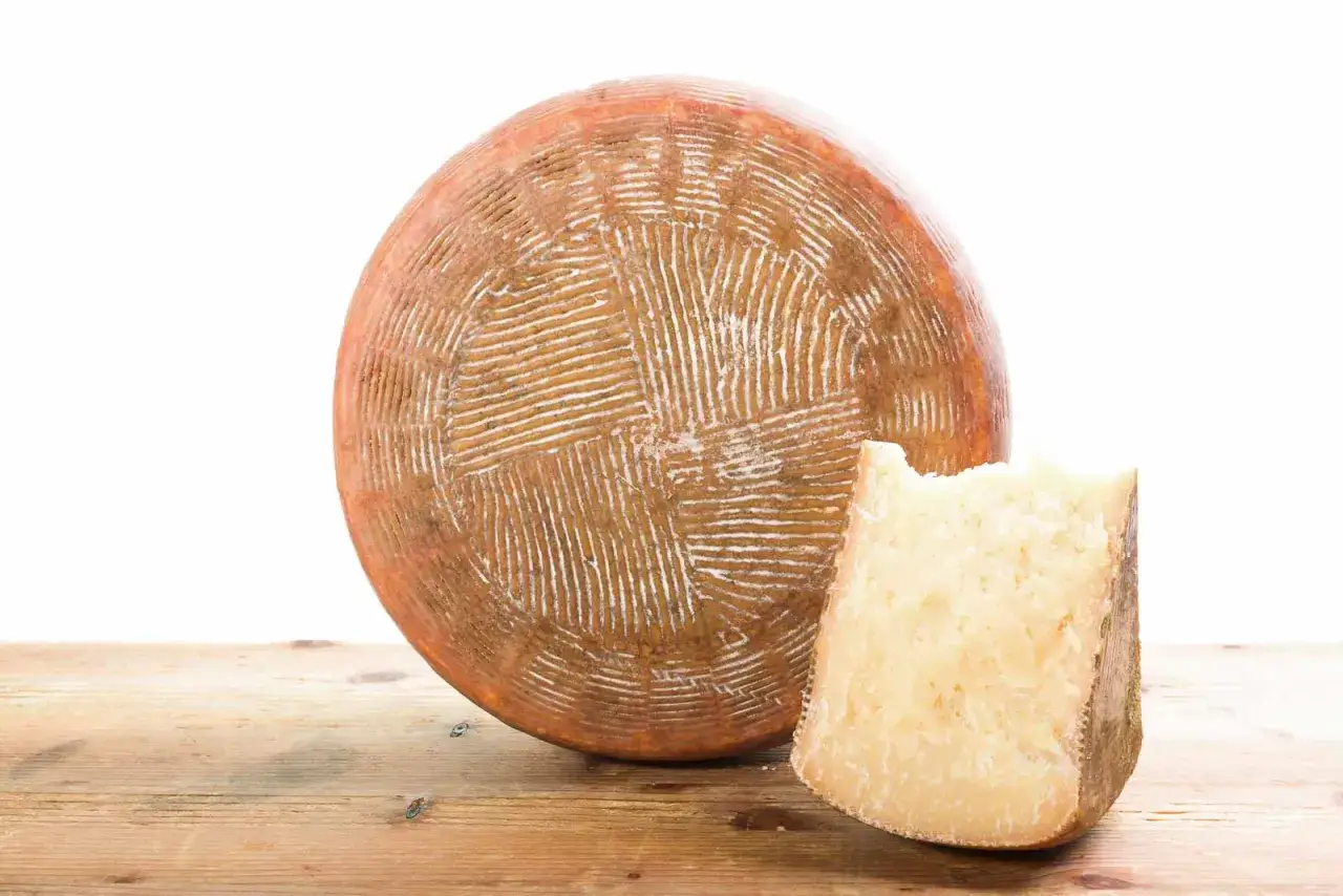 Formaggio pecorino stagionato, perfetto per mangiare a Pienza. Una forma intera e una fetta con un morso.
