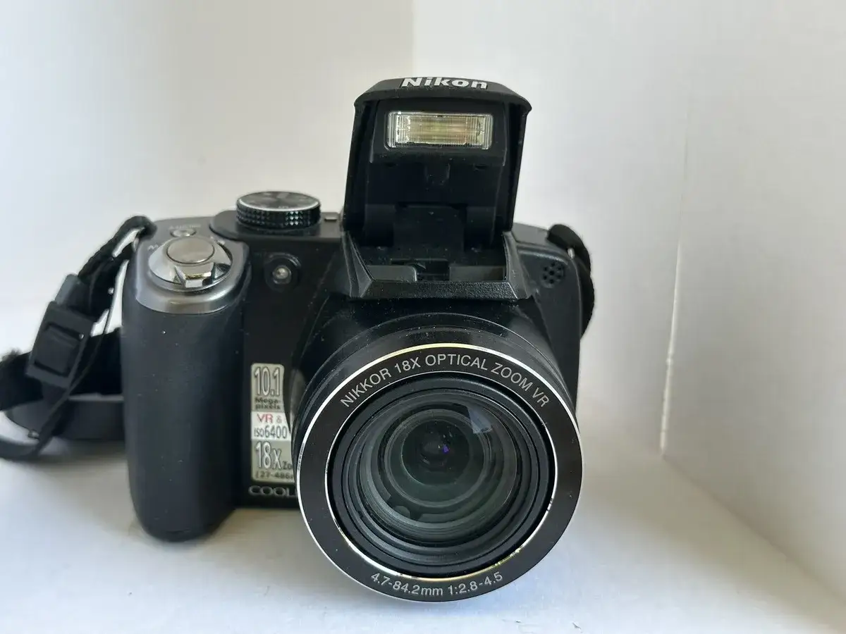 Czarny aparat Nikon p80 z wysuniętą lampą błyskową i obiektywem NIKKOR 18x Optical Zoom VR.