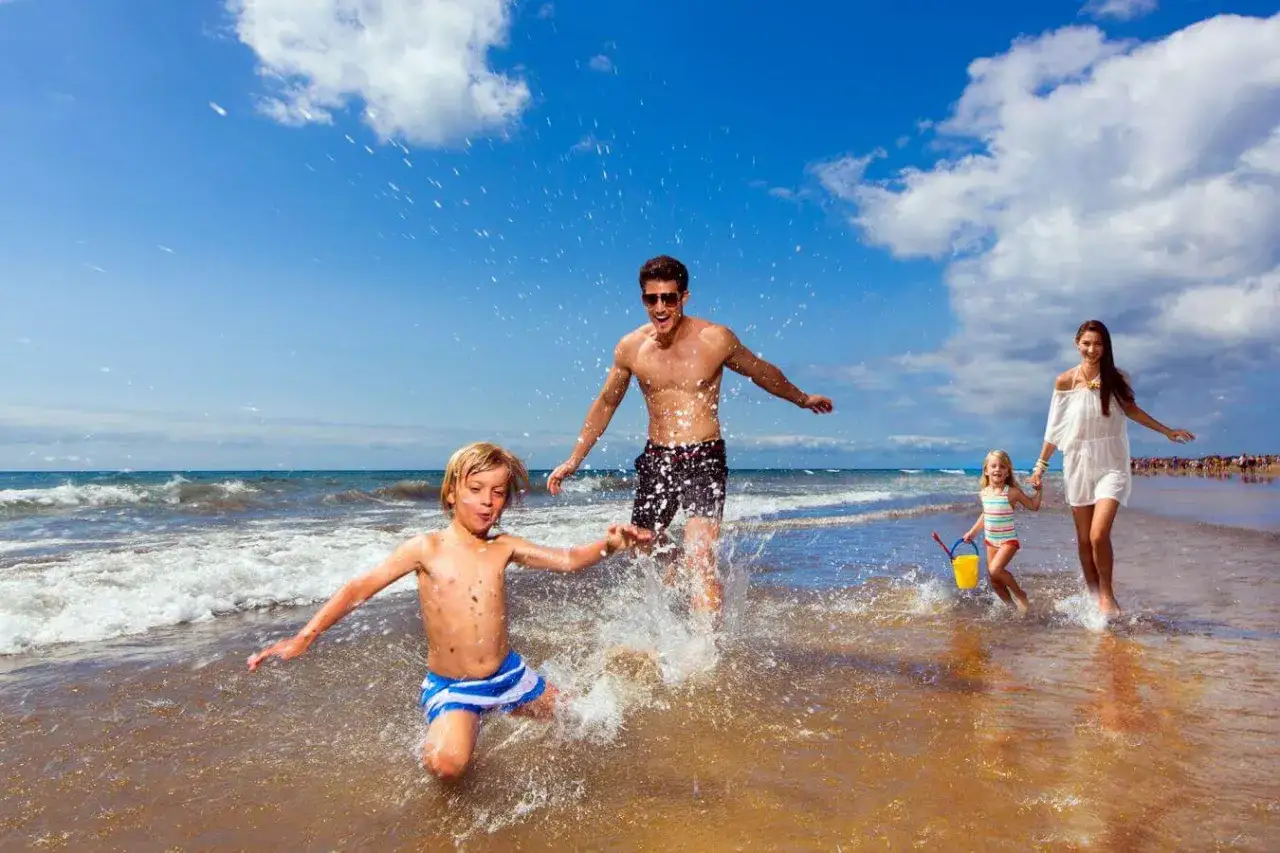 Familia disfrutando de un día soleado en la playa de Gran Canaria con niños, chapoteando en el agua y riendo.