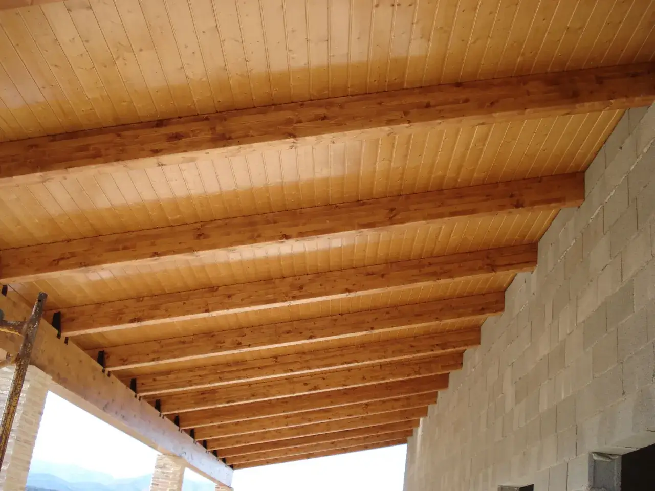 Tejado de madera a un agua, con vigas de soporte y tablones de pino barnizado. Construcci&oacute;n en progreso.