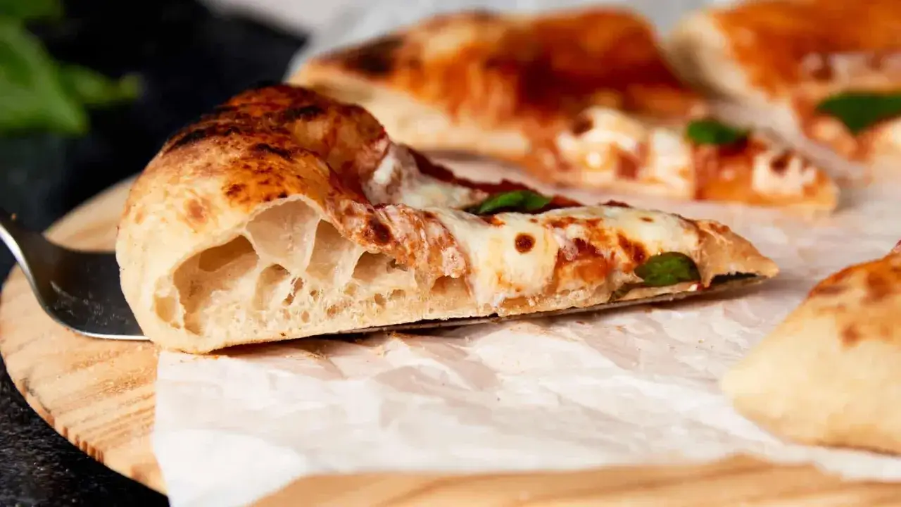 Ein St&uuml;ck neapolitanische Pizza mit luftigem Rand, geschmolzenem K&auml;se und Tomatensauce. Perfekt f&uuml;r ein authentisches neapolitanische Pizza Rezept.