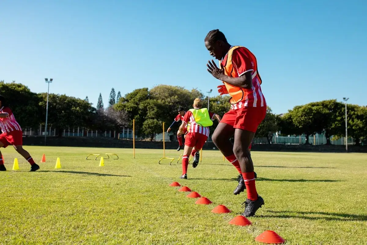 Fu&szlig;baller im Athletik Training, springen &uuml;ber H&uuml;tchen auf einem gr&uuml;nen Feld.