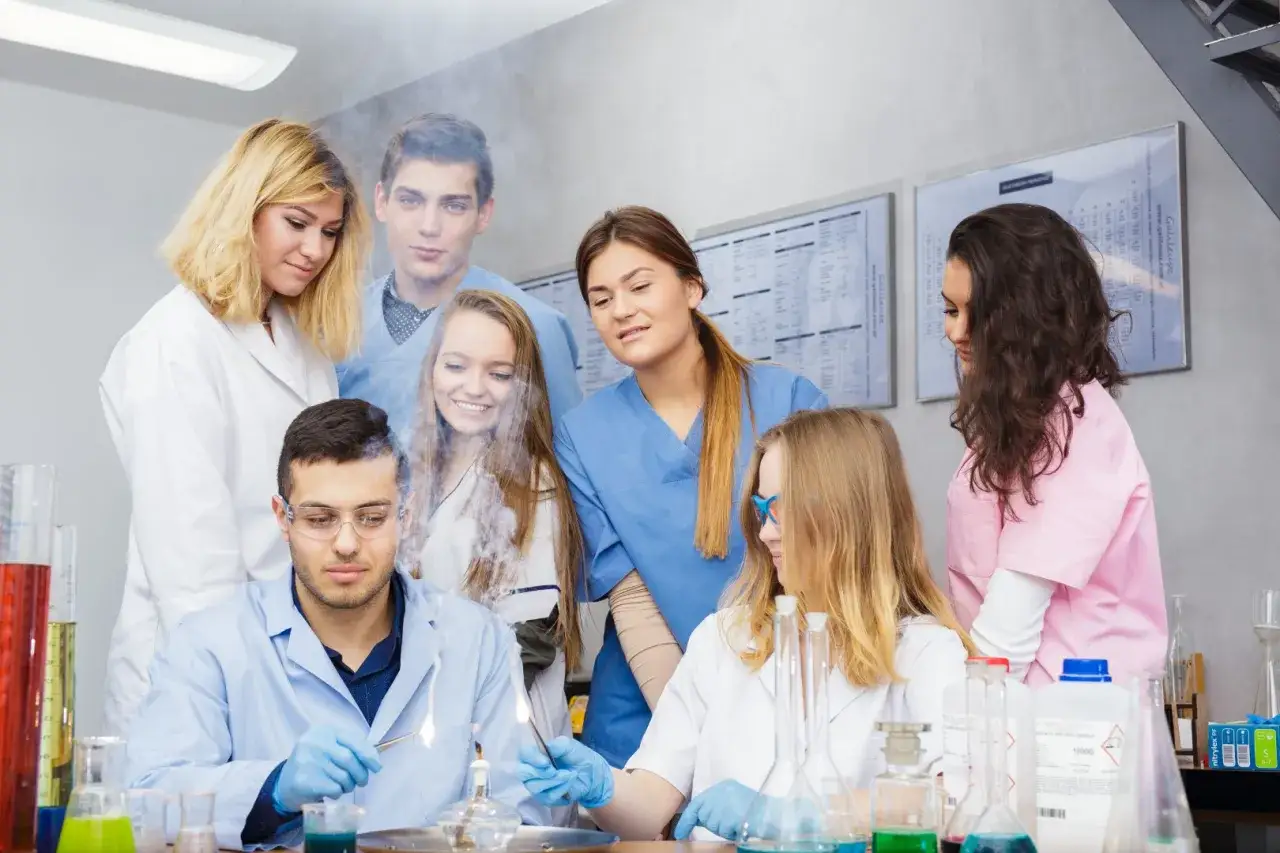 Studenci po biol chemie obserwują eksperyment. Młodzi ludzie w kitlach laboratoryjnych przyglądają się płomieniom i dymowi wydobywającemu się z aparatu.