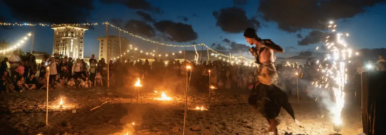Spettacolo di fuoco e fuochi d'artificio su una spiaggia di Rimini, con una folla che assiste a un'esibizione durante un beach party.