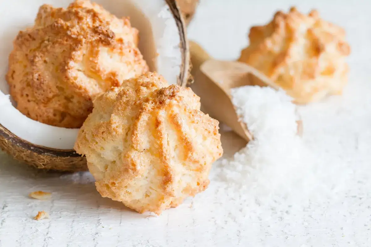 Chrupiące makaroniki na mące migdałowej lub kokosowej, obok połówki kokosa i wiórków.