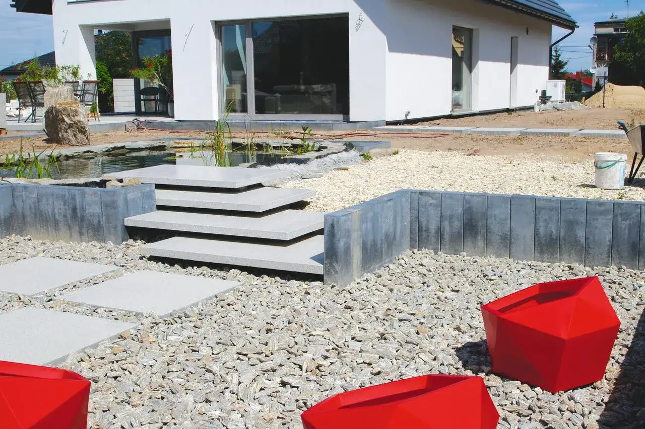 Nowoczesny taras na skarpie z kamiennymi stopniami, oczkiem wodnym i geometrycznymi donicami.