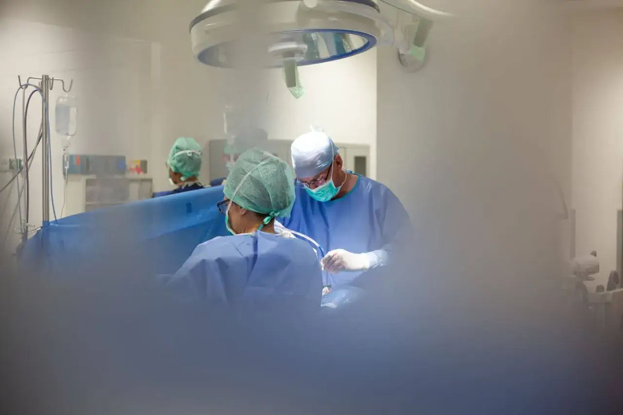 Chirurdzy w maseczkach i czepkach operacyjni pracują przy stole operacyjnym.