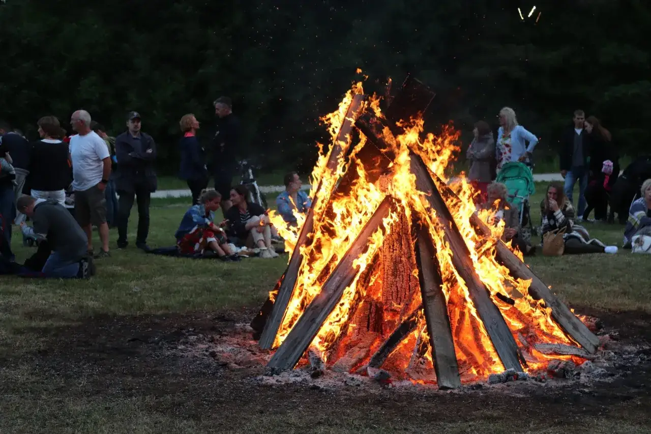 Människor samlas runt en stor midsommarbrasa i Sverige. Värmen från elden sprider sig bland dem som firar.