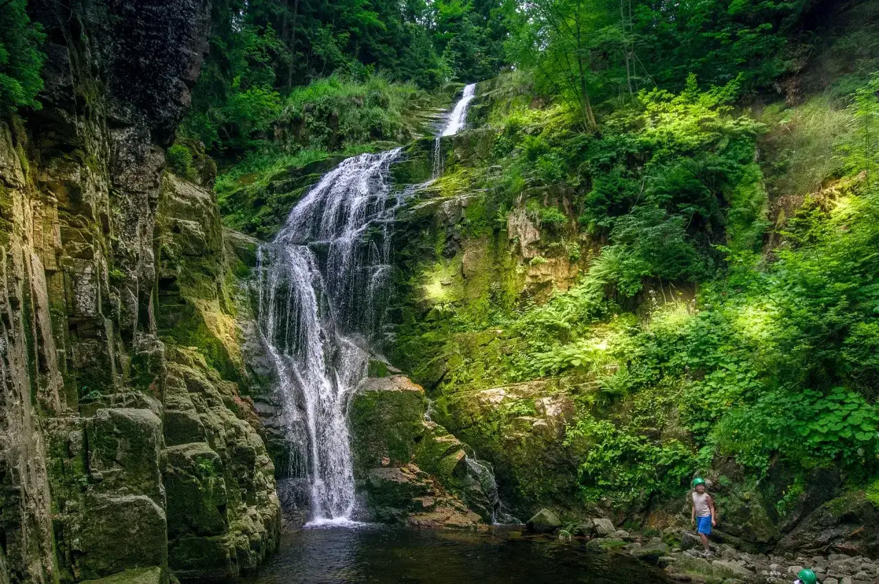 Wodospad w lesie, idealne miejsce na wycieczki dla singli po 50-tce. Dziecko w kasku podziwia piękno natury.