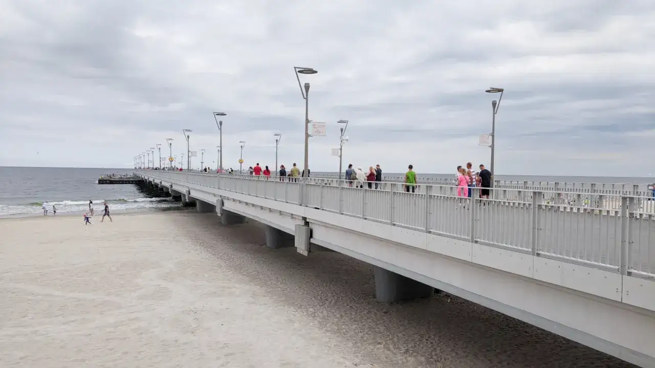 Spacerowicze na molo w Kołobrzegu. Długi deptak nad morzem, z ludźmi spacerującymi i podziwiającymi widoki.