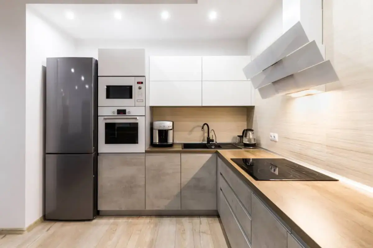Cocina moderna con electrodomésticos integrados, encimera de madera y campana extractora escultural. Una reforma de cocina lista para estrenar.