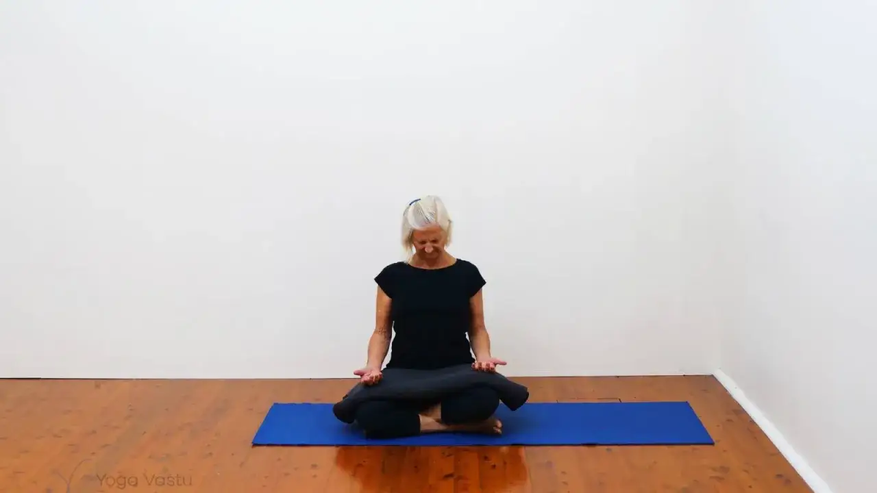 Mujer mayor sentada en postura de loto en una esterilla azul, practicando pranayama que es una técnica de respiración y control de energía vital.